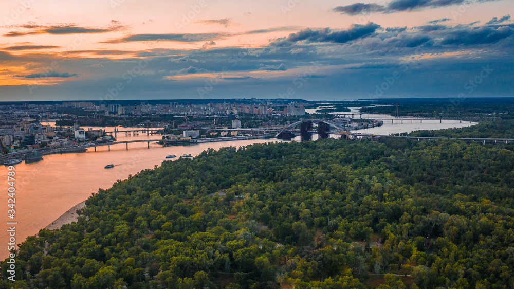 An aerial view is taken with a drone of sunset on summertime in Kyiv (Kiev) city. Skyline with a bridge in construction above the Dniepr river.