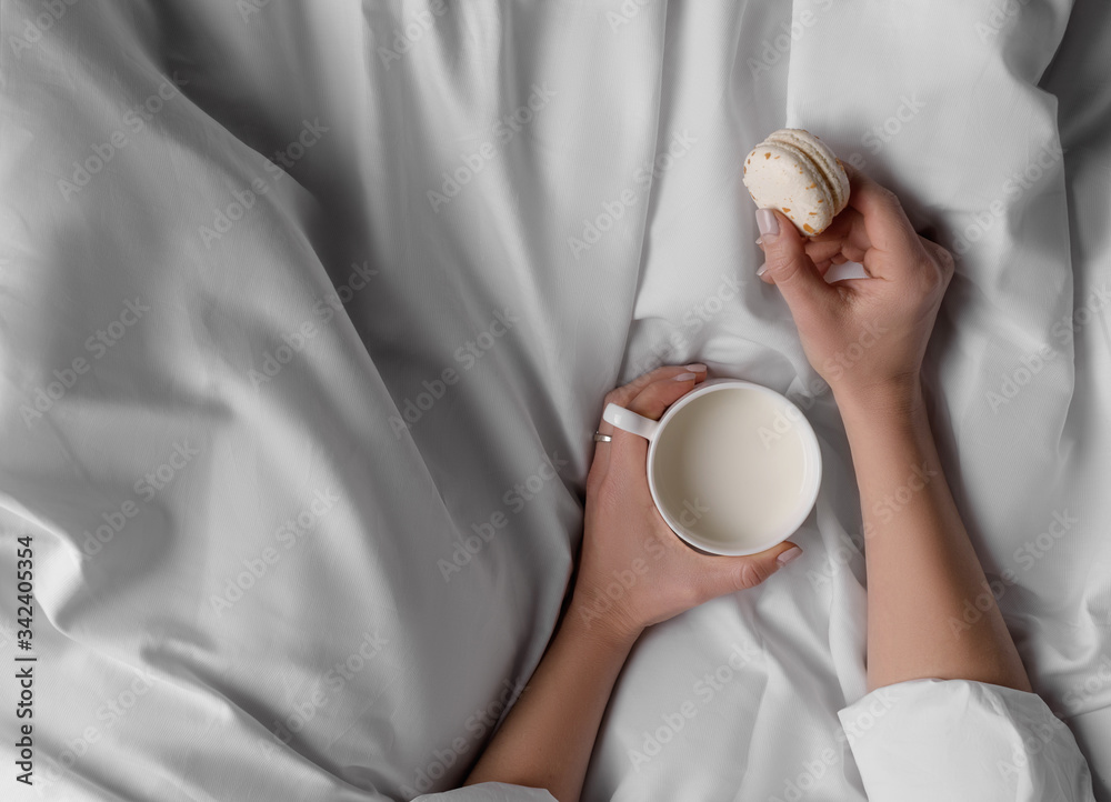woman drinking milk with macaroon in white bedding, breakfast in bed