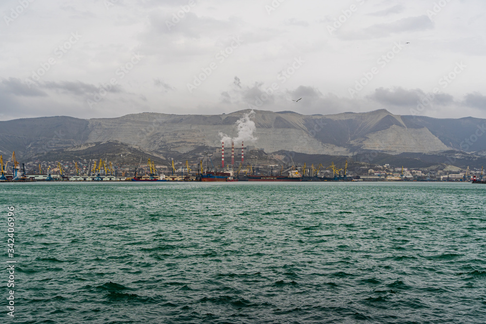 Novorossiysk, Russia - March 25, 2020. - Port cranes along pier of Novorossiysk Commercial Sea Port. Large number of port cranes on blurred background of Caucasus mountains. Selective focus.