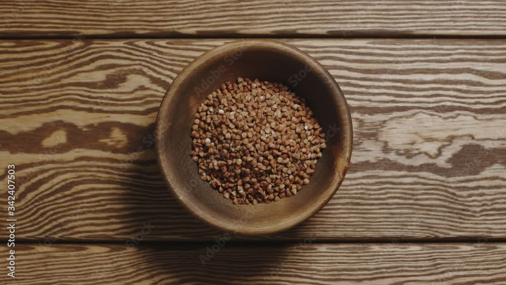 Buckwheats fill a wooden dish. Top view, stop motion. Buckwheats fill a wooden dish. Top view, stop motion.