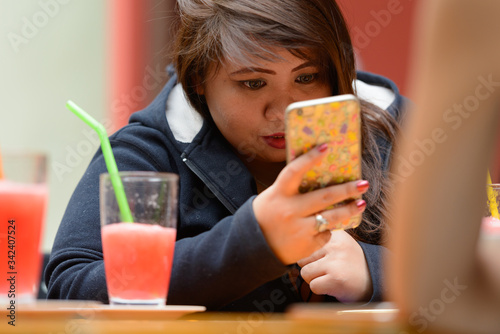 Young Asian woman with friends using phone at the coffee shop outdoors