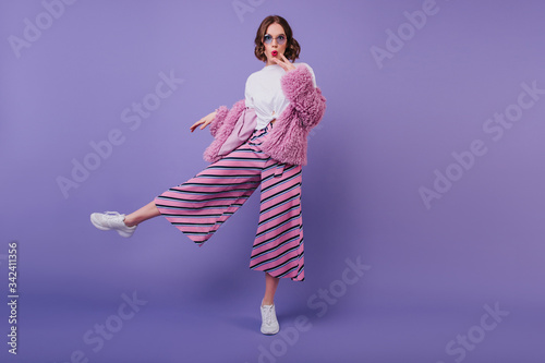 Bilde på lerret Surprised lovely girl in white shoes posing on purple background during indoor photoshoot