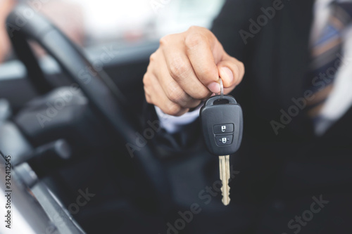 Car key, businessman handing over gives the car key to the other woman on showroom background. © methaphum