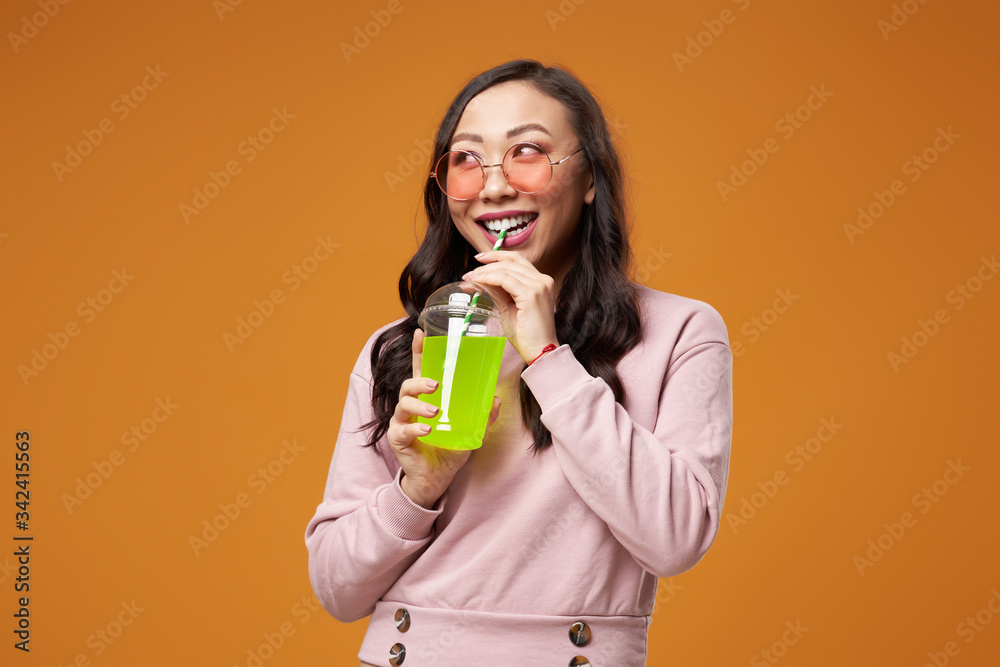 Happy woman in pink glasses with cocktail on empty yellow background Happy woman in pink glasses with cocktail on empty yellow background