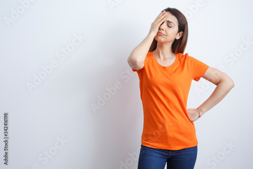 Giovane e bella ragazza con i capelli lisci, indossa una T-Shirt Arancione  disperata si mette la mano in faccia , isolata su sfondo bianco photo