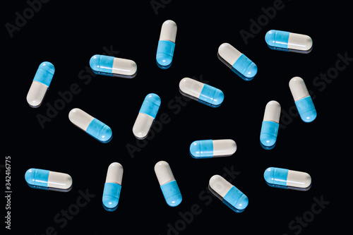 Flat Lay of many blue and white two-piece capsules on an isolated black background. Top view