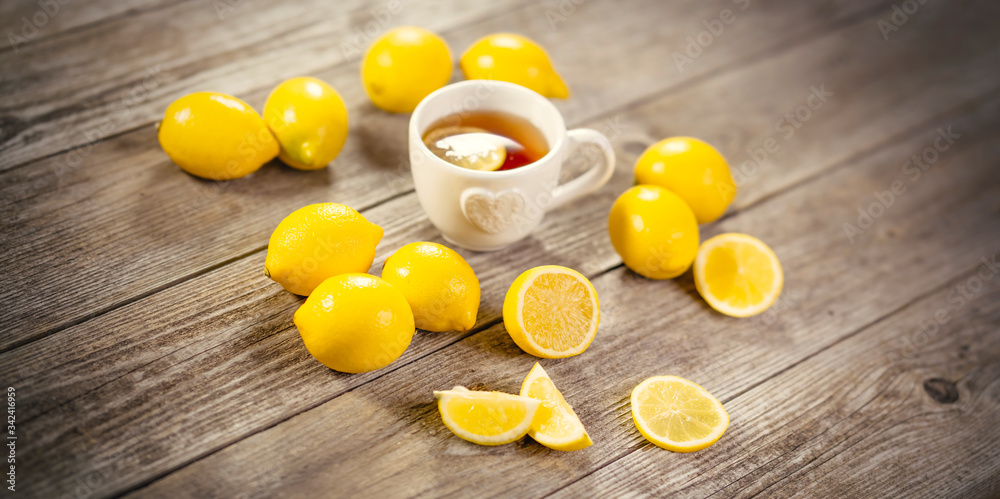 Cup of black tea with lemon slice and plenty of lemons around on grey wooden table. Warm drink infusion for cold fall and winter days. Concept of prevention for flu cold with Vitamin C Cup of black tea with lemon slice and plenty of lemons around on grey wooden table. Warm drink infusion for cold fall and winter days. Concept of prevention for flu cold with Vitamin C