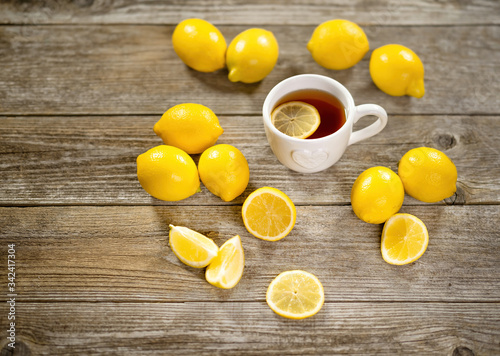 Cup of black tea with lemon slice and plenty of lemons around on grey wooden table. Warm drink infusion for cold fall and winter days. Concept of prevention for flu cold with Vitamin C