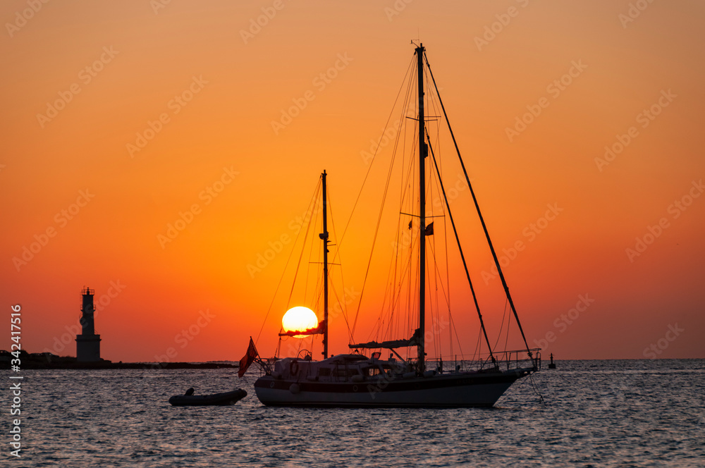Sailboats at sunset anchored in the bay near the lighthouse. Fantastic sunset over the Mediterranean sea in the island of Formentera Spain