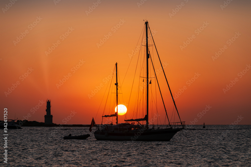 Red sky in a sunset over the sea, the silhouettes of a lighthouse and sailboats. Formentera island, Spain, travel vacation concept