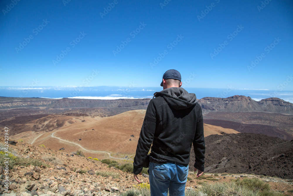 Young man on top of a mountain with amazing panoramic view. Success. Male hiker enjoying the beautiful view from the top. The volcano El Teide in Tenerife, Spain.