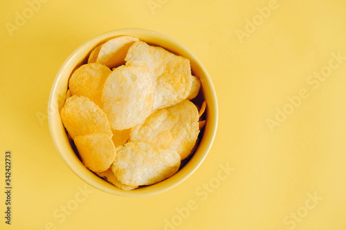 Potato chips in a yellow bowl on a yellow background. Top view. Copy, empty space for text