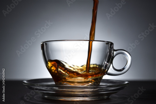 Pouring coffee on a transparent cup on black background