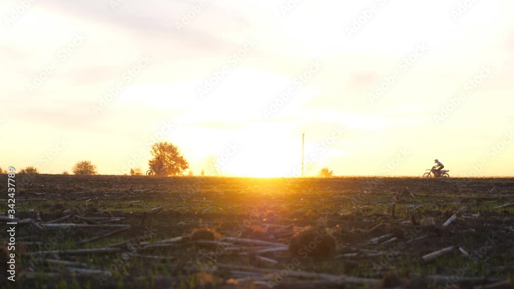 Two motorcyclists riding fast on their motorbikes through field against sunset. Friends having active rest outdoor driving powerful motorcycles at dusk. Bikers enjoying trip. Extreme sport concept Two motorcyclists riding fast on their motorbikes through field against sunset. Friends having active rest outdoor driving powerful motorcycles at dusk. Bikers enjoying trip. Extreme sport concept