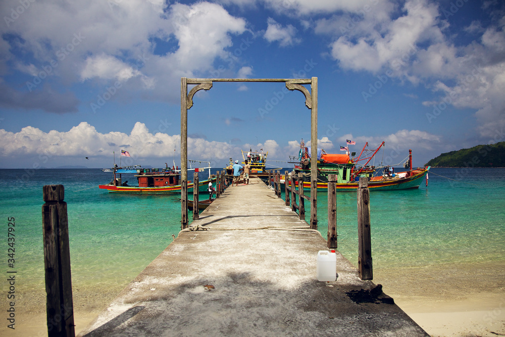 The colorful fishing boats near the pier on the beautiful seashore with crystal clear water. Perhentian Besar island, Malaysia. Sunny day, heat, vacation, tour to Asia. The colorful fishing boats near the pier on the beautiful seashore with crystal clear water. Perhentian Besar island, Malaysia. Sunny day, heat, vacation, tour to Asia.