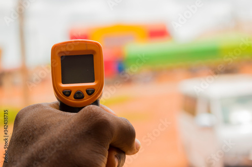 Close-up shot of a man ready to use infrared forehead thermometer (thermometer gun) to check body temperature for virus symptoms - epidemic virus outbreak concept