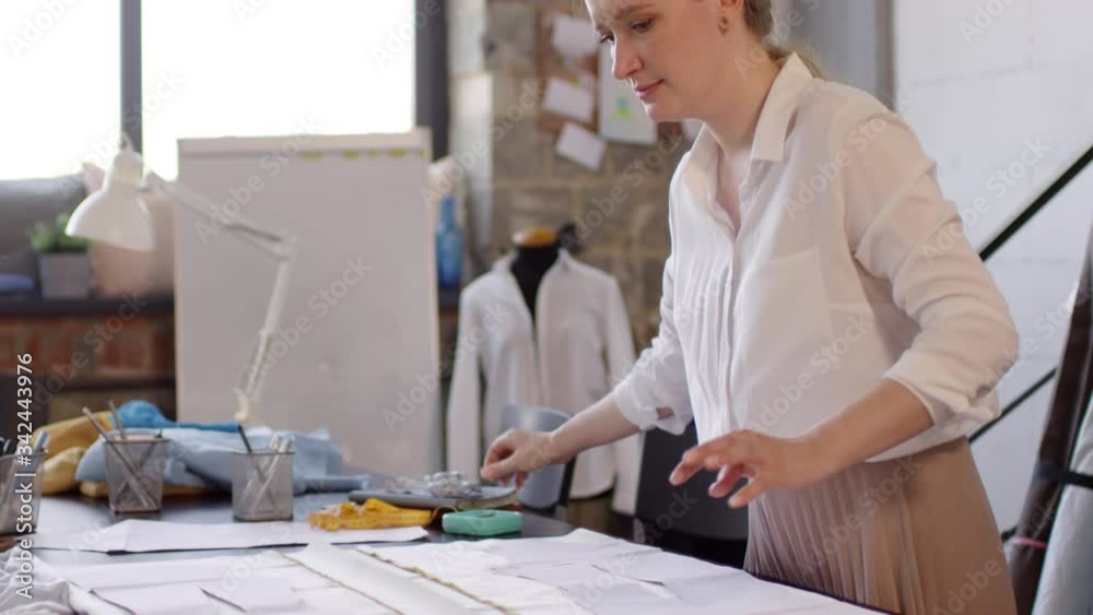 Tilt up of caucasian female dressmaker pinning paper patterns to fabric ...