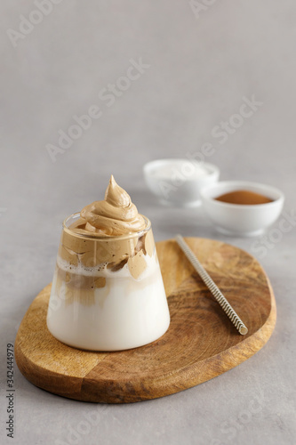 Korean drink. Homemade dalgona coffee in glass with milk on grey background. Trendy fluffy creamy whipped coffee. Wooden stand.