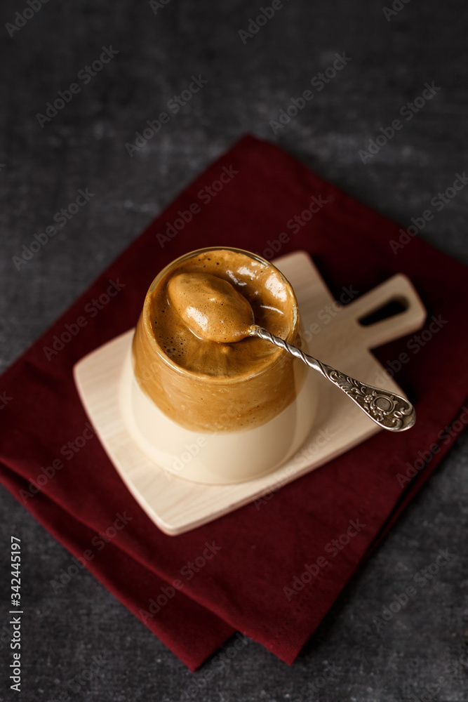 Homemade dalgona coffee in glass with milk on dark background. Trendy fluffy creamy whipped coffee on wooden stand. Korean drink. Homemade dalgona coffee in glass with milk on dark background. Trendy fluffy creamy whipped coffee on wooden stand. Korean drink.