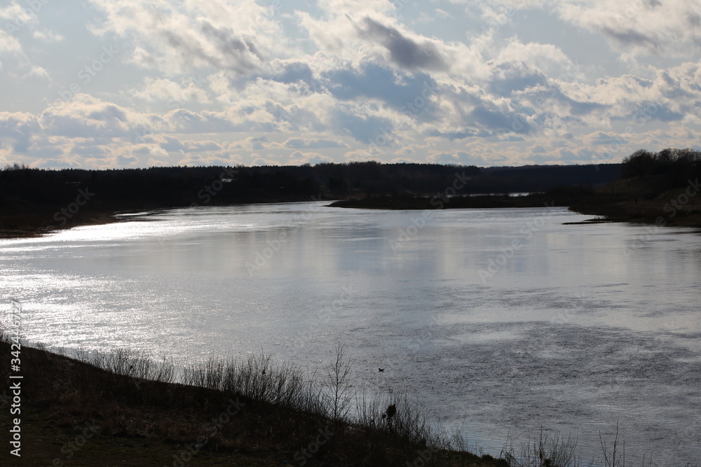 An image of a winding river with silvery shimmering water at dusk under a pale blue sky with ethereal fluffy clouds on the horizon at the end of the day.Water expanses of the Volga river.Russia