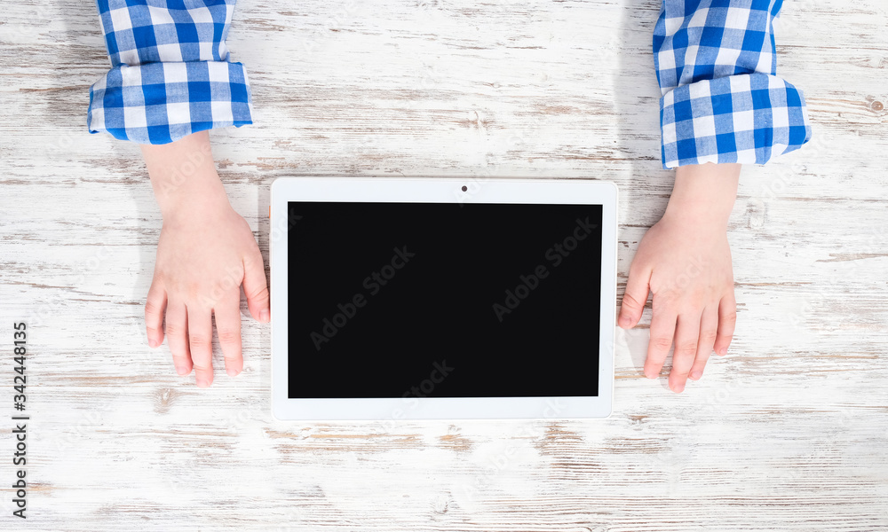 Hands with a tablet. The child plays a tablet at the table. Hands with a tablet. The child plays a tablet at the table.
