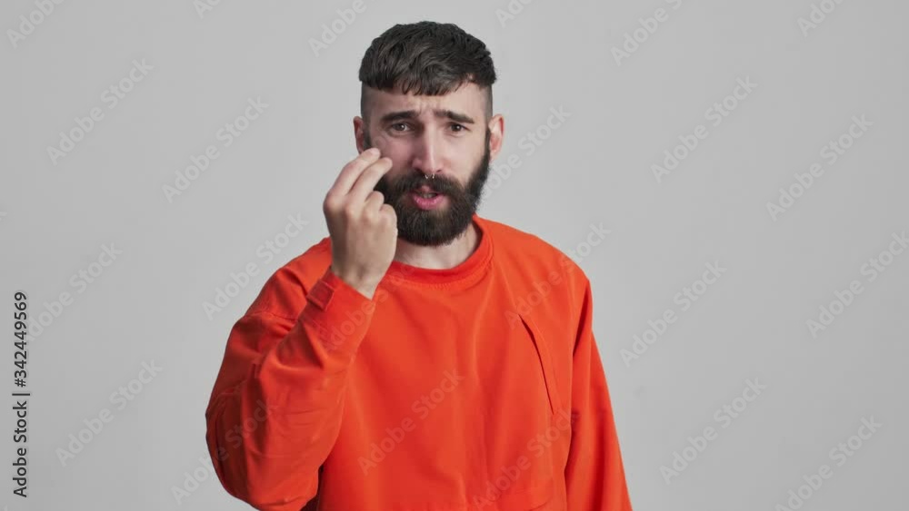 Young handsome negative serious brunette man isolated over grey wall background talking to you. Young handsome negative serious brunette man isolated over grey wall background talking to you.