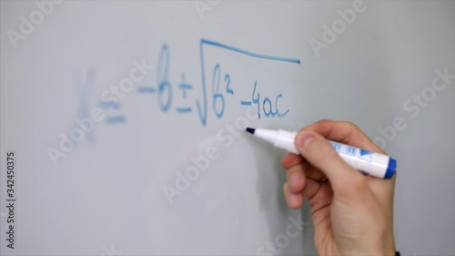 hand with marker pen on whiteboard creating a maths quadratic equation in close up.
