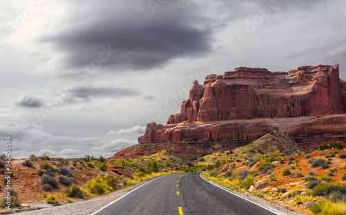 The road passing through the Arches National Park against the backdrop of a stormy sky and mountain landscape.