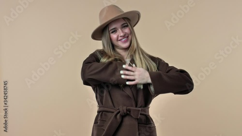 A pretty nice young woman wearing hat and coat is showing a middle finger gesture isolated over the beige background in studio