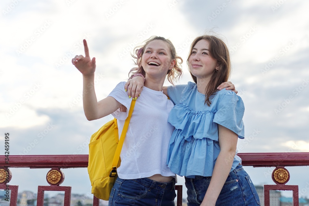 Portrait of two teenage girls friends walking and talking on sunny summer day
