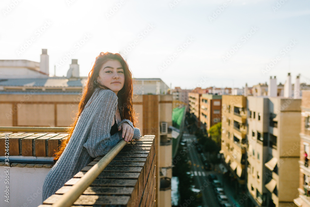 portrait of a beautiful redheaded teenager leaning against the terrace railing with the sun behind her