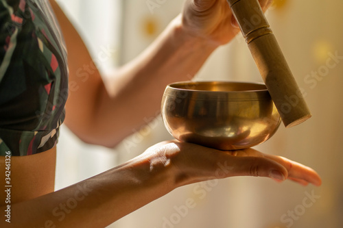Young yogin woman holding a tibetan bowl in the beautiful and gentle light of morning during a yoga session, creating a meditative state through music.