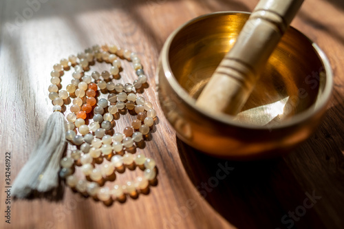 Handmade sacred mala seed beads and a golden Tibetan bowl on a wooden background in the soft and beautiful light of morning, a perfect time for a yoga session acompanied by healing sounds. photo