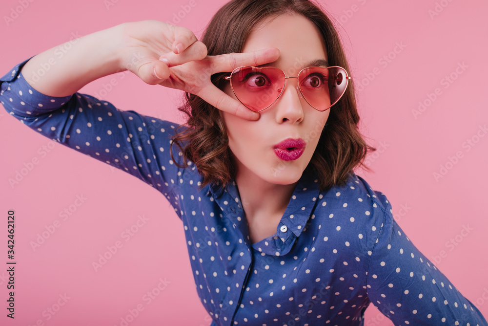Surprised female model in heart glasses posing with kissing face expression. Good-humoured dark-haired girl having fun in studio. Surprised female model in heart glasses posing with kissing face expression. Good-humoured dark-haired girl having fun in studio.