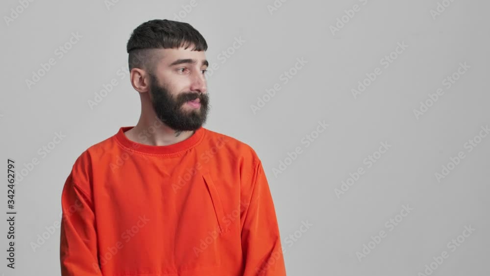 Young handsome cheery happy bearded brunette man isolated over grey wall background pointing aside.
