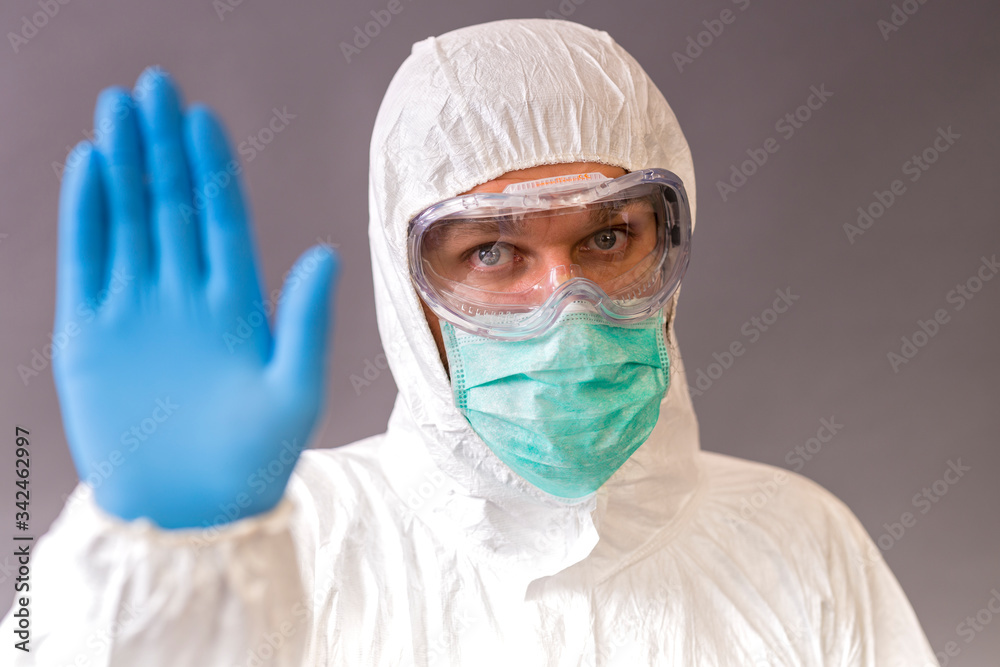 Male doctor with surgical mask, goggles and protective suit showing stop on gray backround. Male doctor with surgical mask, goggles and protective suit showing stop on gray backround.