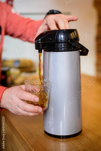 Pouring from thermos into glass american coffee.
