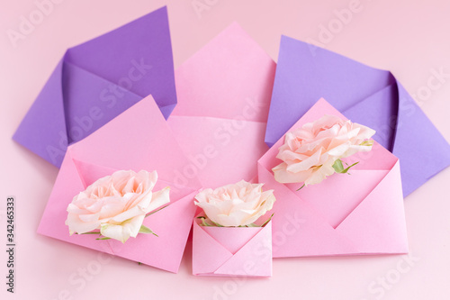 Purple and pink paper open envelopes with full small rose flowers on color background. Spring, summer concept. Romance, love notes, greeting card for March 8 International Woman's, Valentine's day