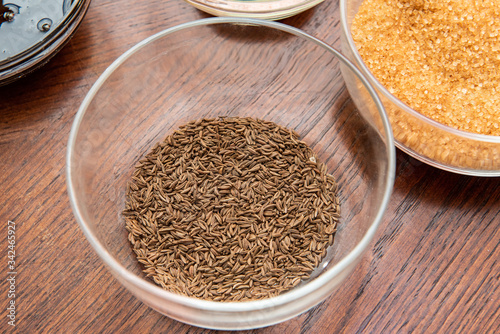 cumin seeds in a glass bowl on a wooden table next to other spices