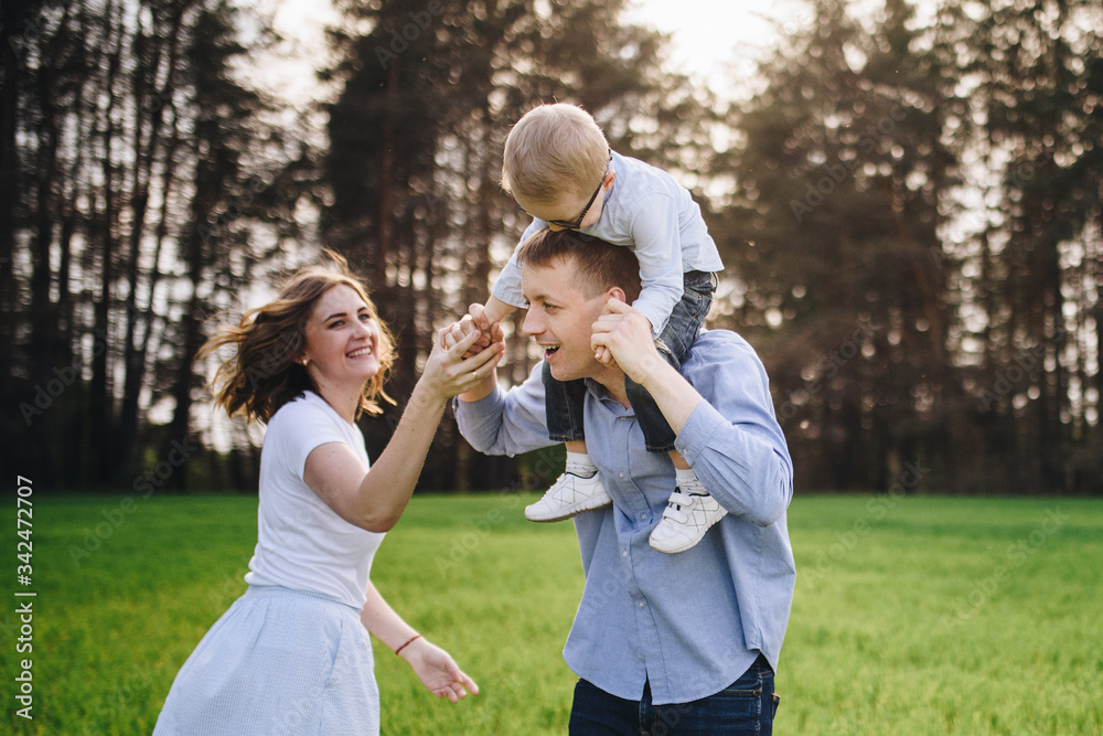 Obraz premium Family in nature. Picnic in the forest, in the meadow. Green grass. Blue clothes. Mom, dad, son with glasses. Boy with blond hair. Joy. Parents play with child. Together. Picnic basket. Food, blanket