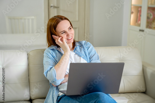 woman on couch using computer. talking by phone