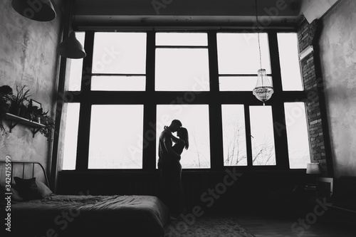 silhouette of young couple standing  and hugging against window background indoors. portrait of young beautiful couple. 