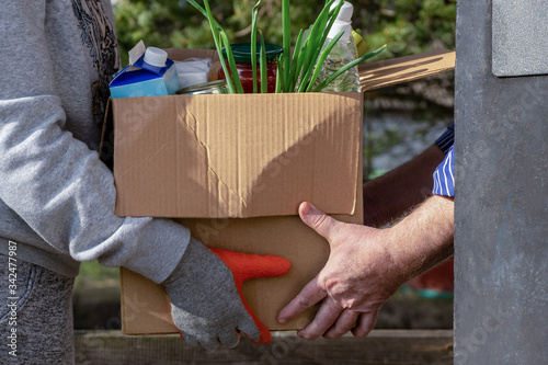 A volunteer passes a box of food to the hands of a man. Home delivery of products.