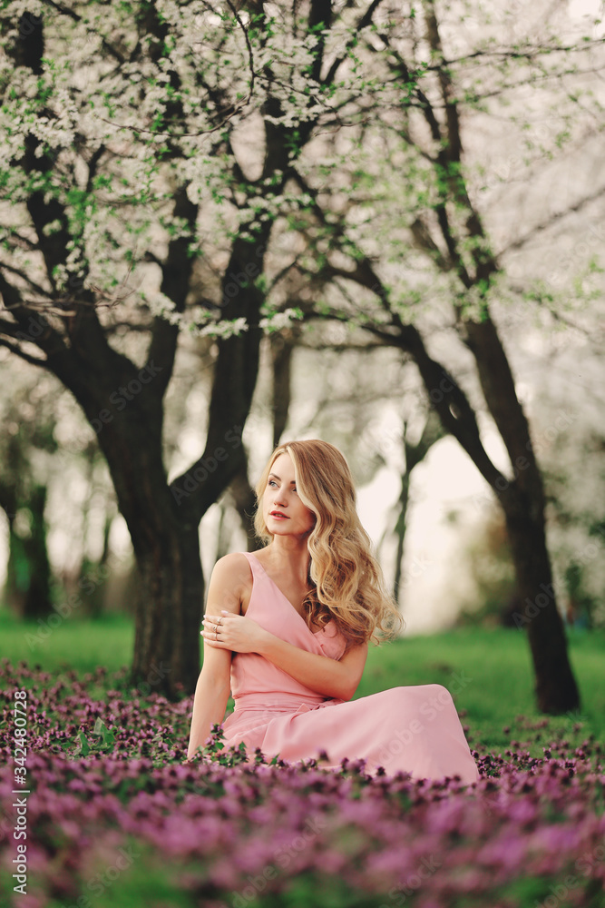 Beautiful blonde young woman in colorful flowers. girl with make-up and hairstyle in pink dress in blossoming spring park. woman's day