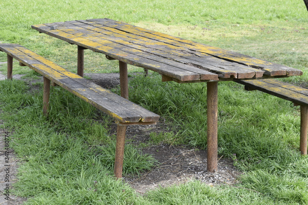 Wooden table and benches on rusty metal pipes. The wooden surface is covered with fungus and moss. Recreation area in nature. Wooden table and benches on rusty metal pipes. The wooden surface is covered with fungus and moss. Recreation area in nature.