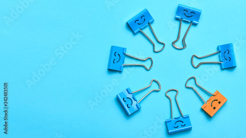 Top view of funny emoji office stationary. Smiling faces on paper binder clips. Blue and yellow office accessories. One object looking different. Team building concept. Successful team communication
