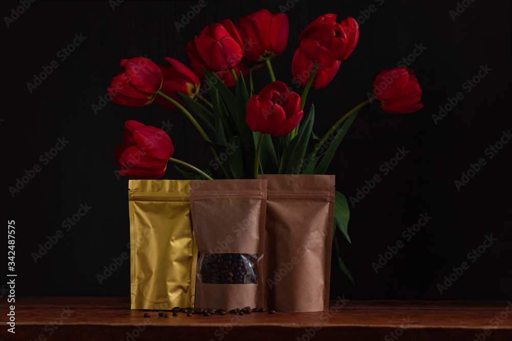 Pouch bags for coffee and tea with amazing blooming red tulips bouquet on black background. Food shop packaging mockup. Foiled metal and kraft paper packs. Dark moody low key flowers banner copy space