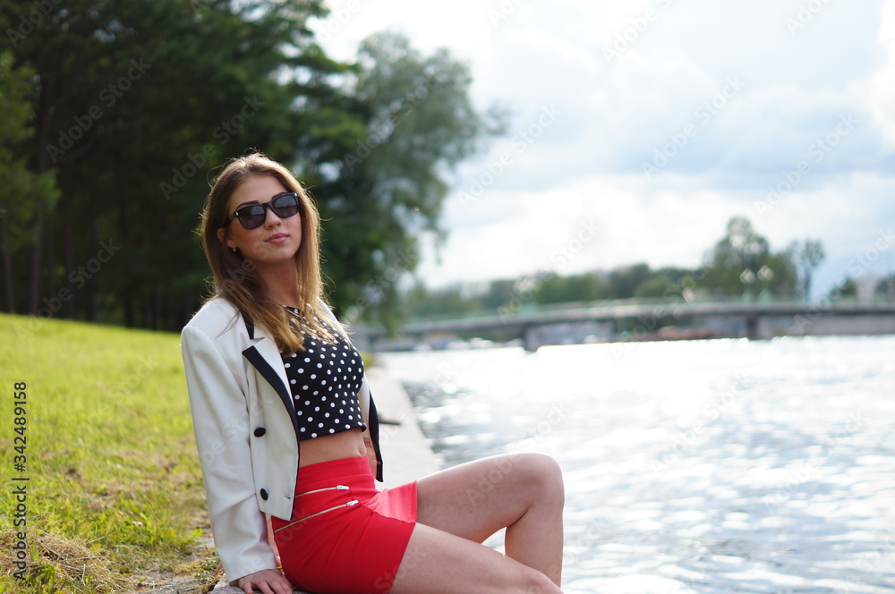 Beautiful and attractive girl is relaxing in the park on a summer day. Dressed and posing like a professional model with glasses and a red skirt