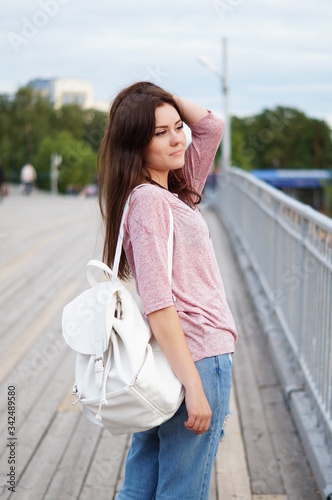 A cute and cute teenager girl is fashionably dressed and she walks in the park with a white backpack. The modern style of society. Freedom of movement. Walk in the park