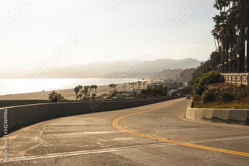 Calle costera con vista al océano pacifico. Playa de Santa Monica, California. Paisaje costero con playa, palmeras, montañas, bruma y atardecer. photo